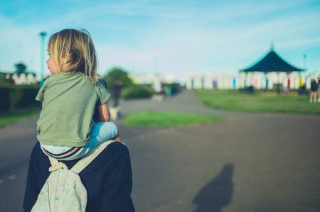 A little toddler is riding on his mother's shoulders at sunset in the parkの写真素材