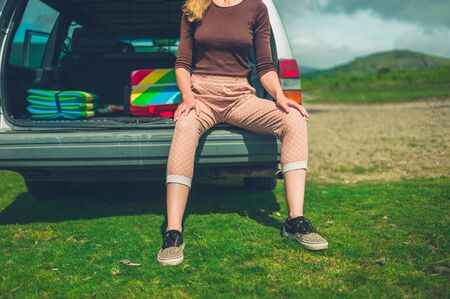 A young woman is sitting in the back of her stationwagon in nature on a sunny summer dayの写真素材