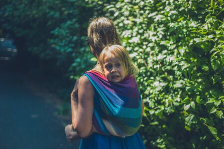 A young mother is carrying a big toddler in a sling on her backの写真素材
