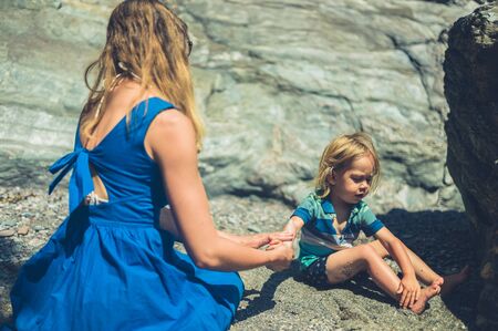 A young mother is on the beach with her toddler and is applying suncream to his skinの写真素材