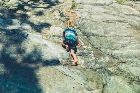 A little toddler is climbing on some rocks in the summer