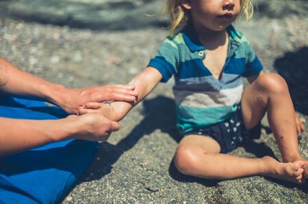 A young mother is on the beach with her toddler and is applying suncream to his skinの写真素材