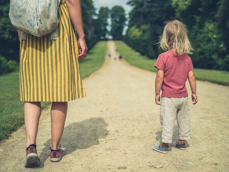A young mother and her toddler are standing on a path in a parkの写真素材