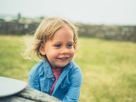 A little toddler is sitting at a picnic table outside by the sea on a foggy day