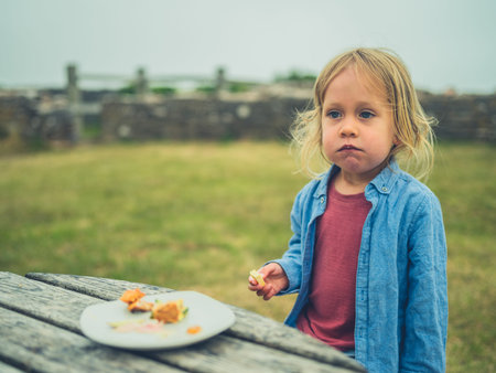 A littlet toddler is eating his lunch at a picnic table outdoors on a foggy dayの写真素材