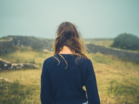 A young woman is standing in a historic field with ruins in the mist