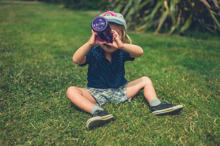 A little toddler is sitting on a lawn and is drinking from a bottleの写真素材