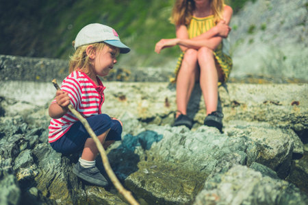 A young mother and her toddler are relaxing on some rocks by the sea in summer