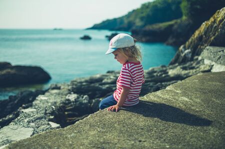 A little toddler is sitting on a rock by the seaの写真素材