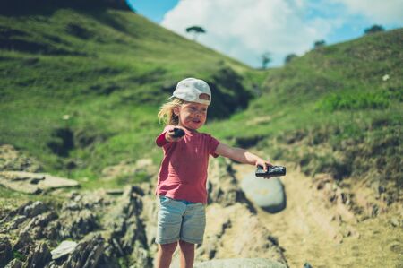 A toddler is standing on the beach with two pieces of charcoal in his handsの写真素材