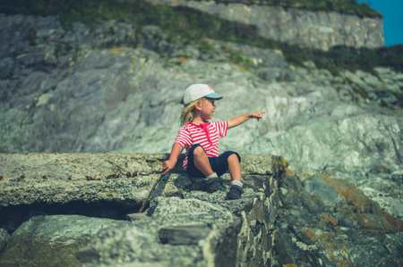 A little toddler is sitting on a rock by the sea
