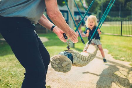 A little toddler is being pushed on a swing by his grandfatherの写真素材