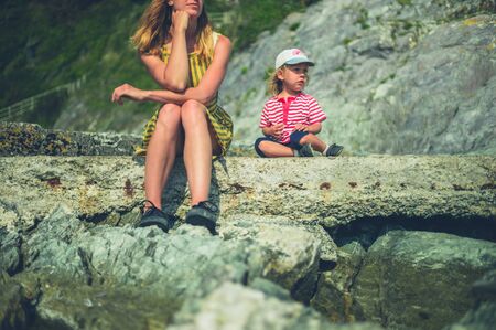 A young mother and her toddler are relaxing on some rocks by the sea in summerの写真素材