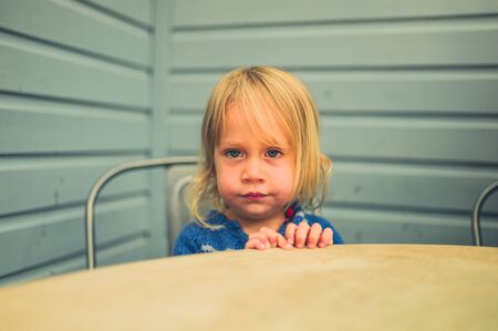 A little toddler is sitting at a table in a cafeの写真素材