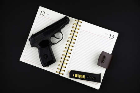 a traumatic pistol and ammunition are lying on an open notebook on a black backgroundの写真素材