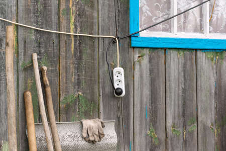 an electric wire with a socket hangs on the wooden wall of the house near the windowの写真素材