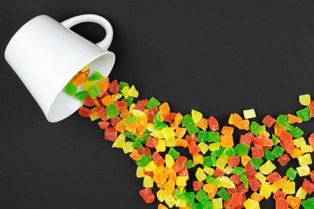 multicolored candied fruits with sugar sprinkled from a white cup on a black backgroundの写真素材