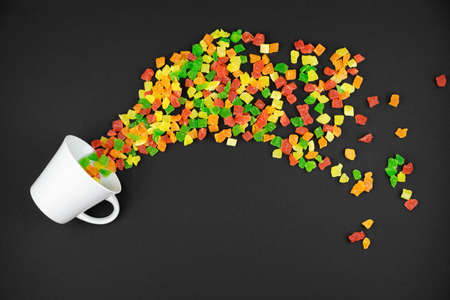 multicolored candied fruits with sugar sprinkled from a white cup on a black backgroundの写真素材