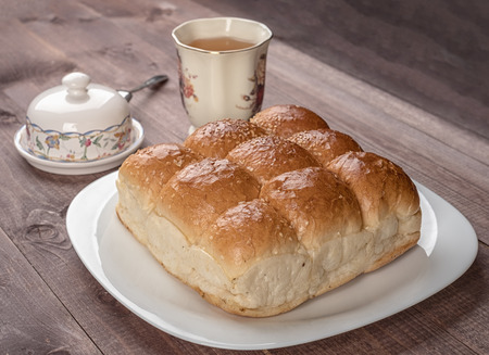 White bread in glass plate, butter dish and cup of tea on wooden tableの写真素材