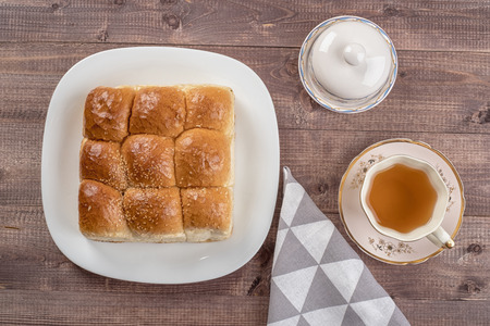 White bread in glass plate, spoon, napkin, butter dish and cup of tea on wooden tableの写真素材