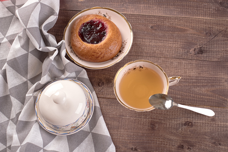 Cake in white plate, napkin, butter dish, spoon and cup of tea on wooden tableの写真素材