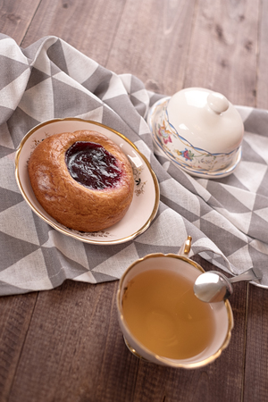 Cake in white plate, napkin, butter dish, spoon and cup of tea on wooden tableの写真素材