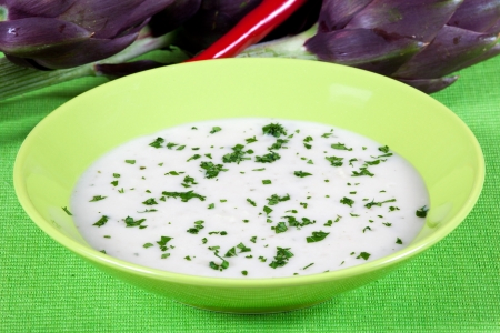 Artichoke vegetarian soup in a dish on a green tableの写真素材