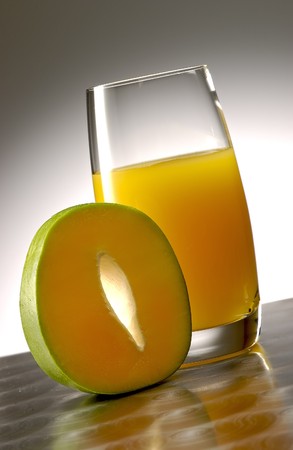Mango juice and half a mango on polished aluminum surface.の写真素材