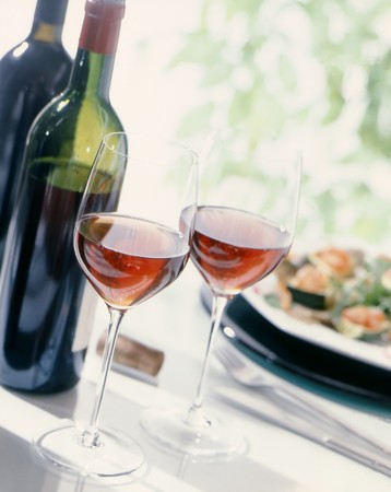 Two wine glasses, along with bottles of wine and a plate with food,の写真素材