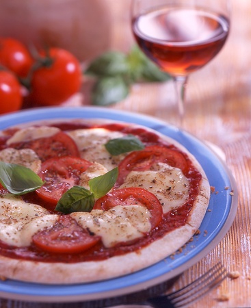 pizza with tomatos, cheese and basil with a glass of red wine in the backgroundの写真素材