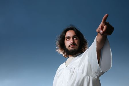 Man looking like Jesus pointing his finger, dramatic blue sky behind.の写真素材