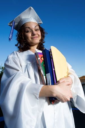 Happy graduate female student holding a big pile of textbooks and foldersの写真素材