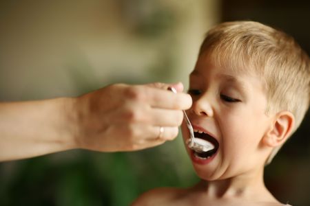 Female hand feeding little boy with spoon of jogurt. Shallow DOF.の写真素材