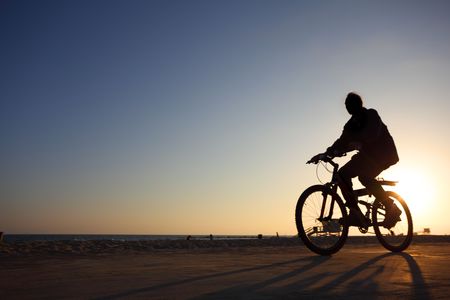 Biker silhouette riding along beach at sunsetの写真素材