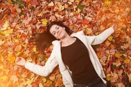 Portrait of beautiful young woman lying on yellow autumn leaves outdoors.の写真素材