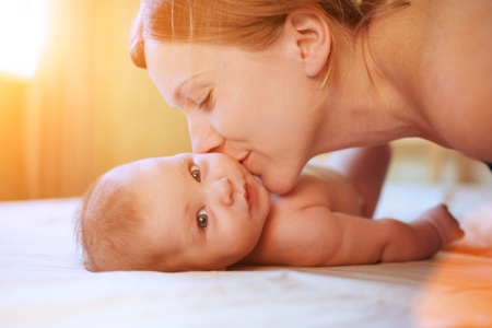Mother kissing baby daughter on sunny background. Closeup, shallow DOF.の写真素材