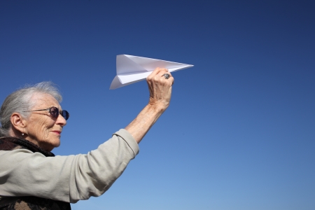 Senior woman playing with paper plane over blue sky.の写真素材