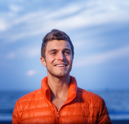 Portrait of handsome happy active young adult man in orange jacket outdoors の写真素材