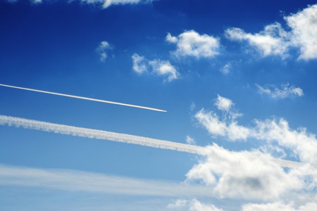 Jet trails  and white clouds over blue sky backgroundの写真素材