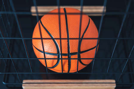 New, orange basketball ball located in a metal basket on a dark surface.の写真素材
