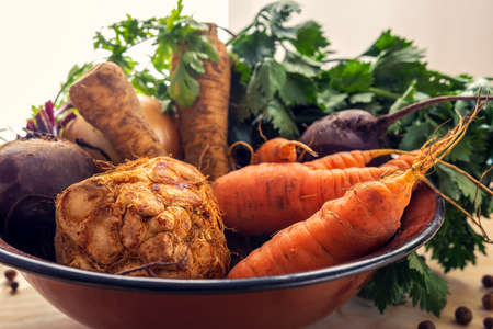 Old, brown bowl full of organic - planted vegetables: carrots, parsley, celery, onions and beetroots placed on a table made of plywood. Fresh, healthy, raw food.の写真素材