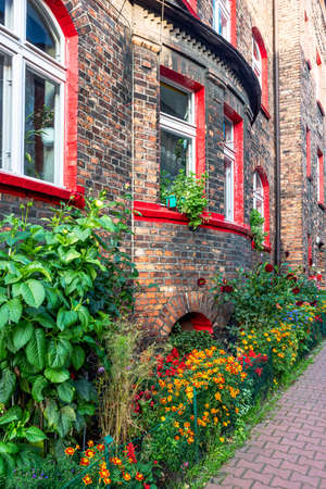 Facade of an old, traditional, silesian brick block house in Nikiszowiec, Katowice, Poland. Small, colorful garden in front of the building.の写真素材