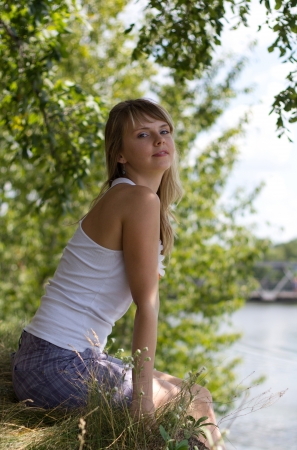 The beautiful girl sitting on the bank of the river on a sunny dayの写真素材