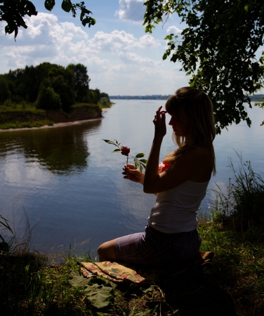 The beautiful girl sitting on the bank of the river on a sunny dayの写真素材