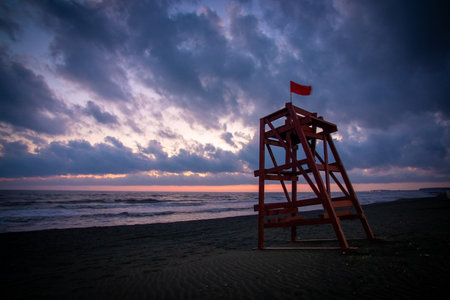 A lifeguard tower stands on a beach with a red flag for safetyの写真素材