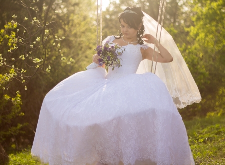 Portrait of a beautiful bride in white wedding dress sitting on swing outdoorsの写真素材