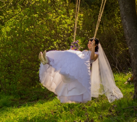 Portrait of a beautiful bride in white wedding dress sitting on swing outdoorsの写真素材