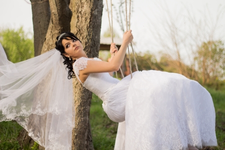 Portrait of a beautiful bride in white wedding dress sitting on swing outdoorsの写真素材