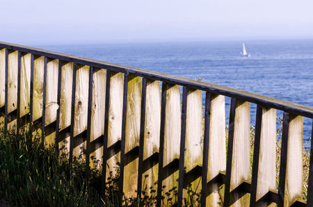 WOODEN FENCE LOOKING TO THE SEA WHERE A SAILBOAT IS INTUED IN THE DARK