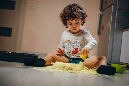 little boy playing with yellow kinetic sand on the floor at homeの写真素材